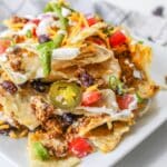 A plate of loaded nachos topped with cheese, ground meat, jalapeños, beans, sour cream, tomatoes, and green onions.