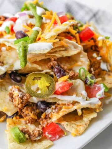 A plate of loaded nachos topped with cheese, ground meat, jalapeños, beans, sour cream, tomatoes, and green onions.