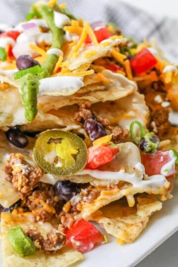 A plate of loaded nachos topped with cheese, ground meat, jalapeños, beans, sour cream, tomatoes, and green onions.