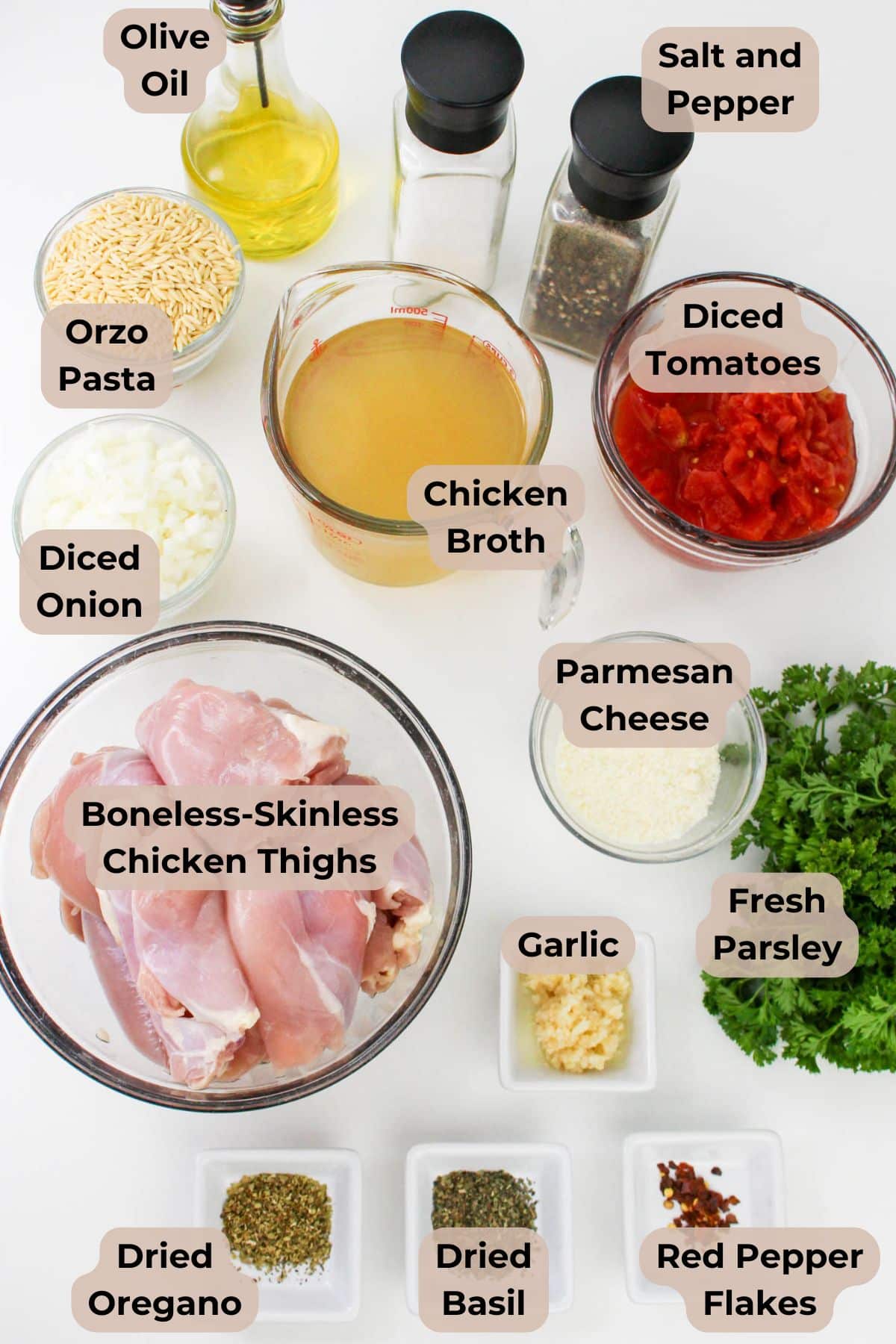 Baked chicken and orzo, surrounded by a medley of spices, herbs, diced tomatoes, cheese, chicken broth, oil, and seasonings arranged on a table.