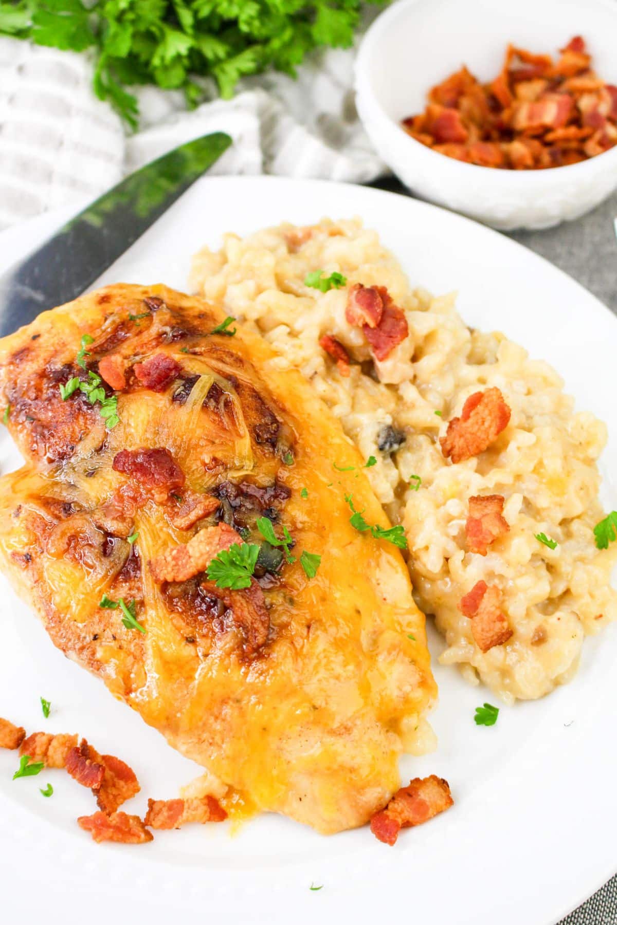 Cheesy chicken with crispy bacon, served with creamy risotto on a white plate.