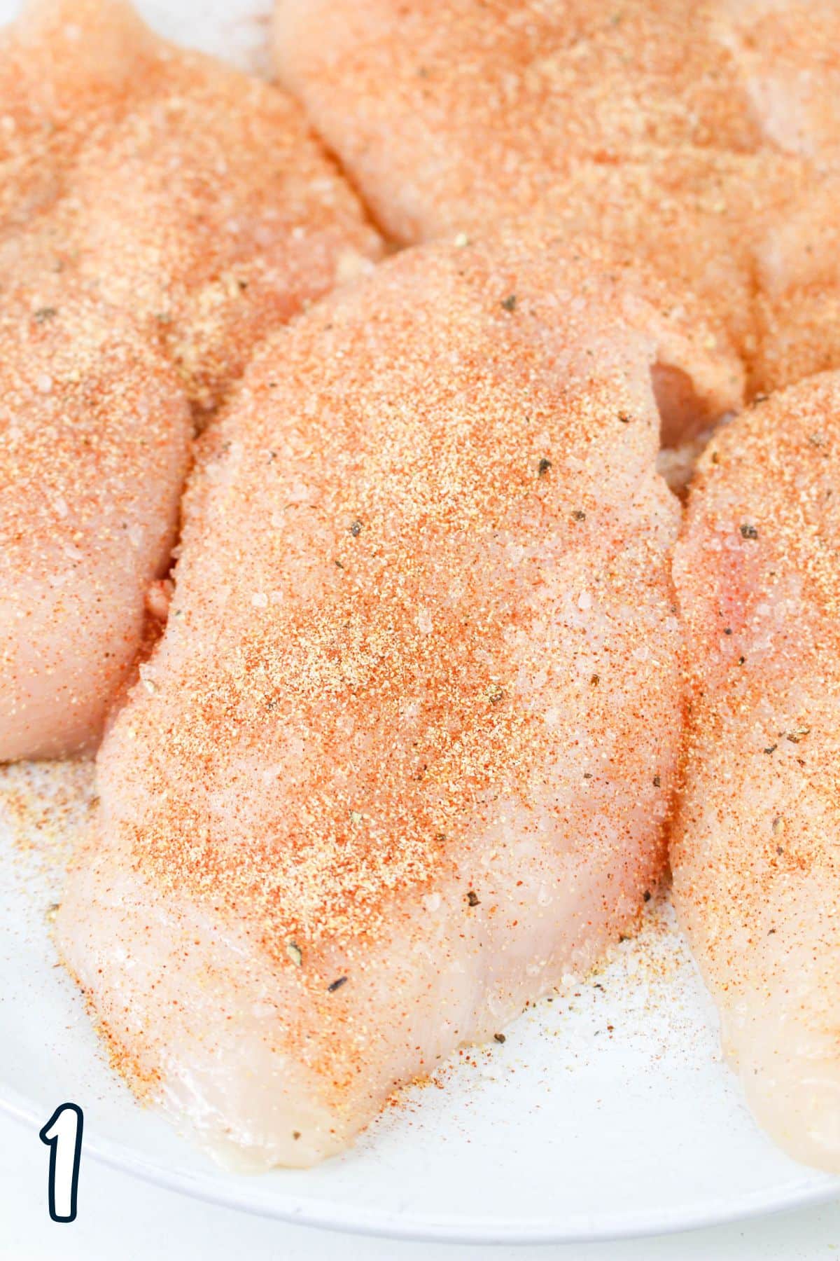 Raw chicken breasts seasoned with spices on a white plate.