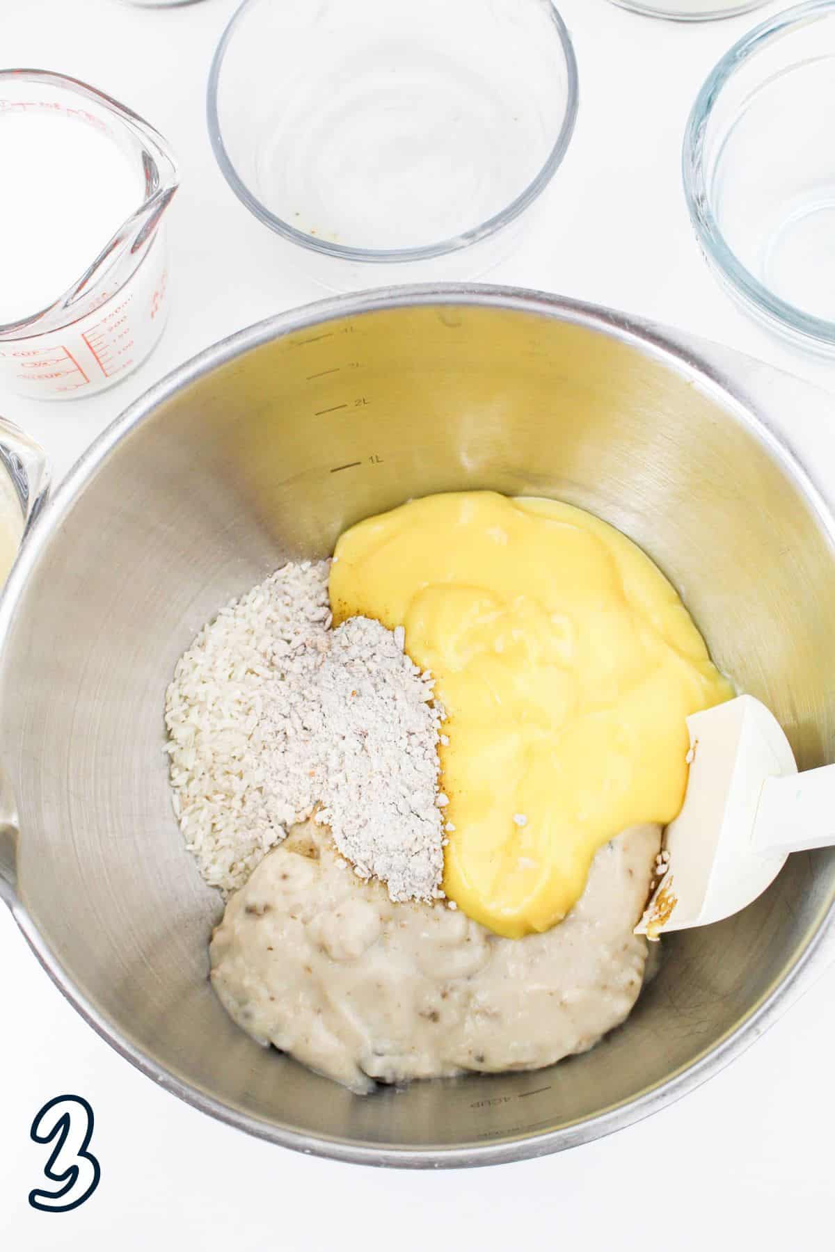 Mixing bowl with rice, sauce, and another ingredient being combined with a spatula; measuring cups nearby.