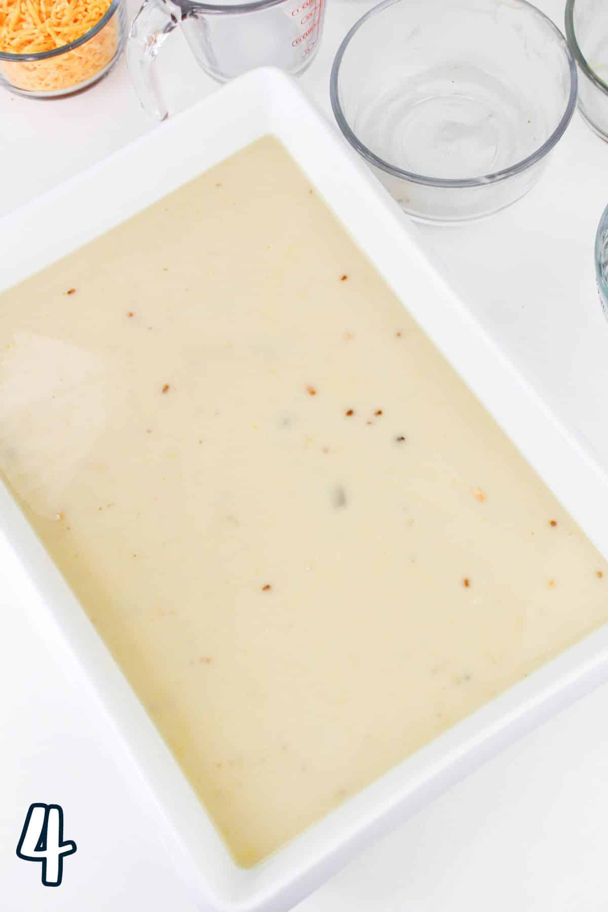 A white baking dish filled with cream sauce, surrounded by empty bowls and a numbered "4" in the corner.