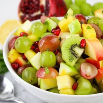 A bowl of colorful fruit salad with grapes, kiwi, apple, pineapple, and pomegranate seeds.