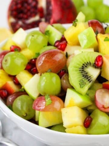 A bowl of colorful fruit salad with grapes, kiwi, apple, pineapple, and pomegranate seeds.