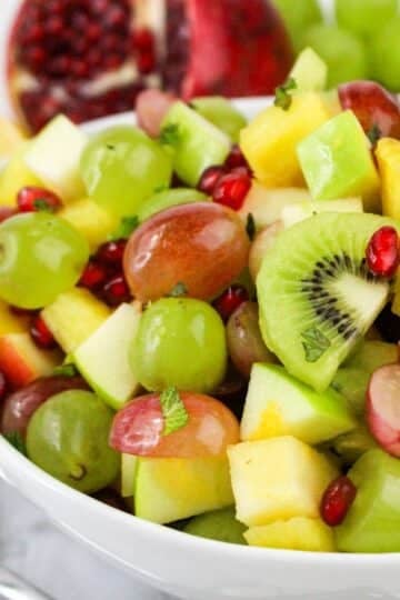 A bowl of colorful fruit salad with grapes, kiwi, apple, pineapple, and pomegranate seeds.