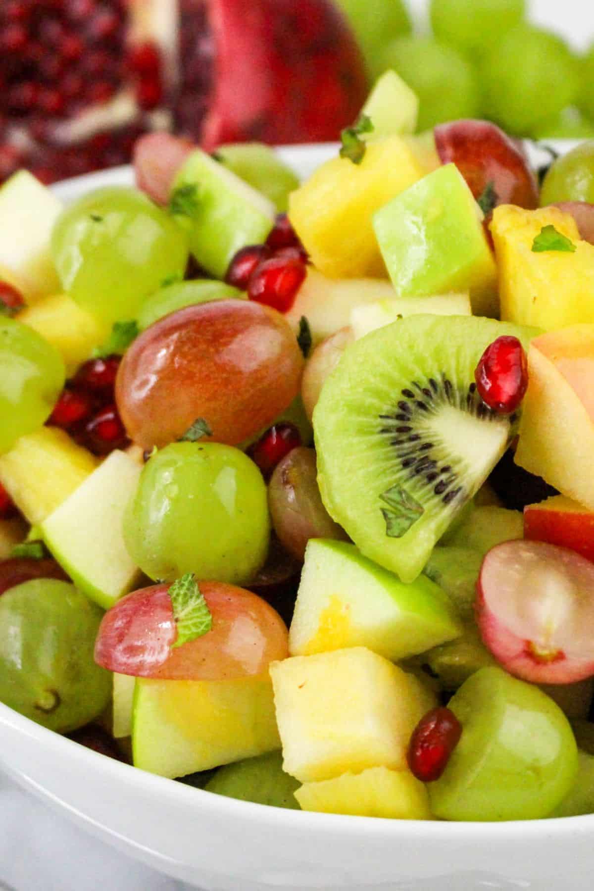 A bowl of fresh fruit salad with grapes, kiwi, apple, and pomegranate seeds.