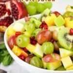 Bowl of colorful fruit salad with grapes, kiwi, apples, and pomegranate, against a festive backdrop.