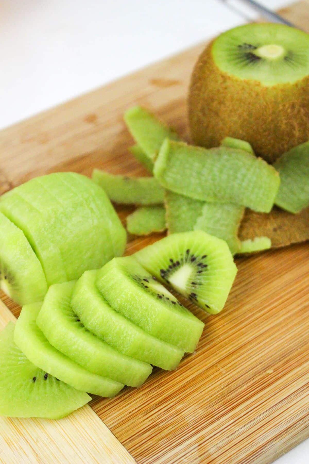 Sliced kiwi with peels on a wooden cutting board.