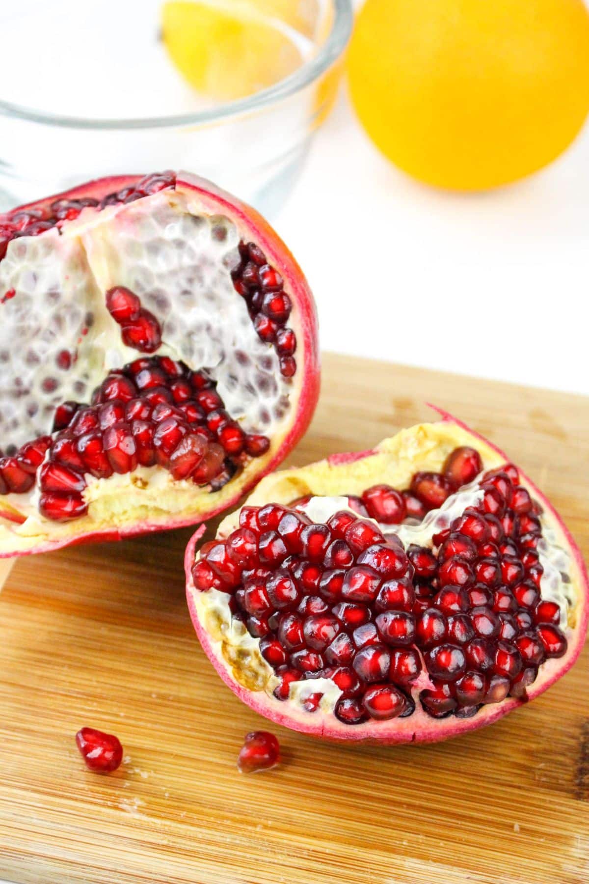 A halved pomegranate with vibrant red seeds on a wooden surface.