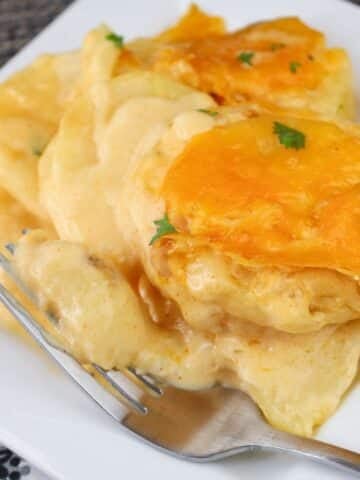 Cheesy scalloped potatoes on a white plate with a fork, garnished with parsley.