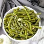 Bowl of cooked green beans with garlic and onions, placed on a gray cloth.