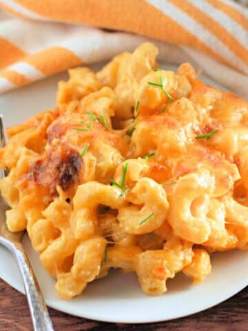 A plate of creamy macaroni and cheese garnished with chives, next to a striped napkin and a fork.