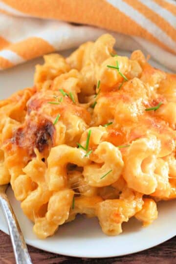 A plate of creamy macaroni and cheese garnished with chives, next to a striped napkin and a fork.