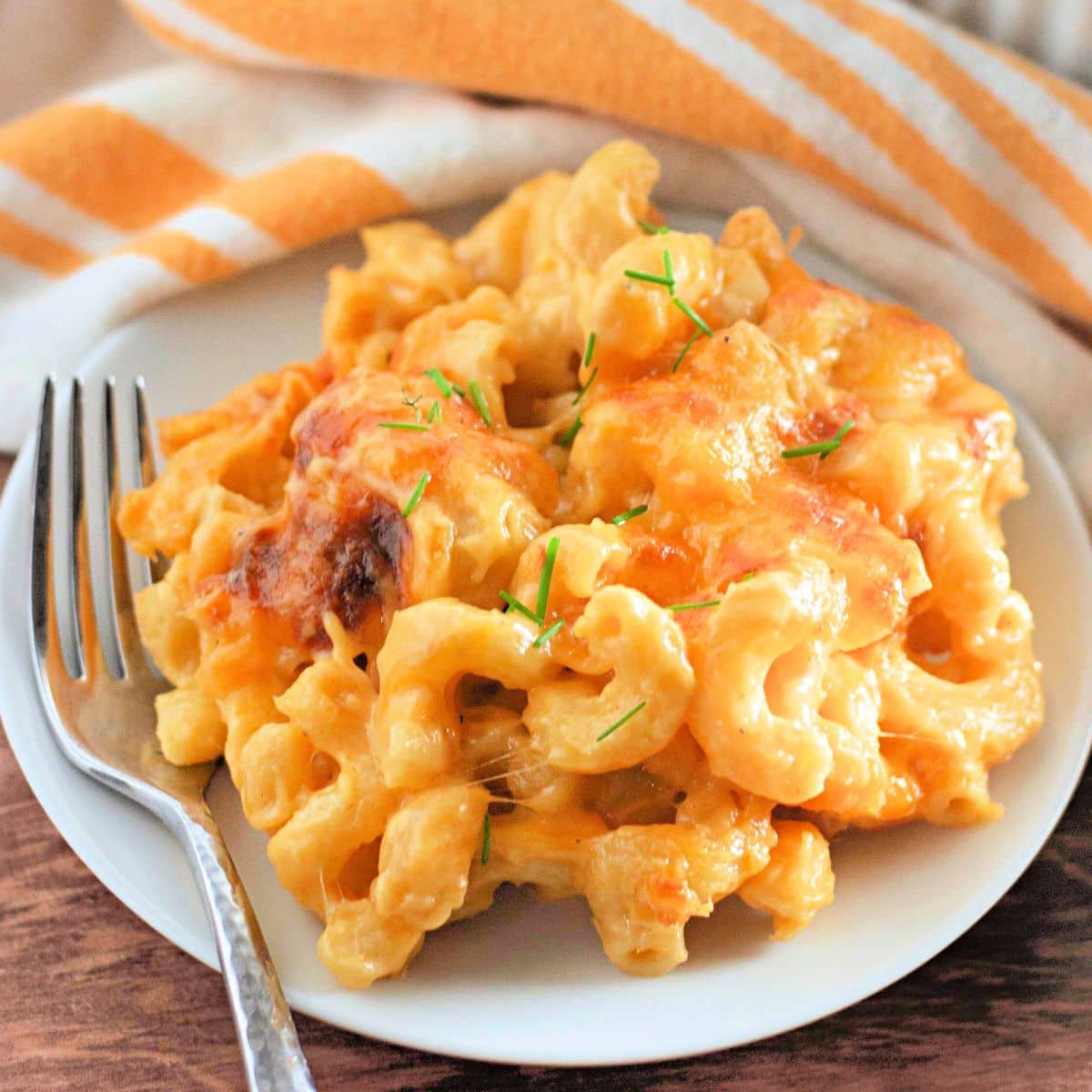 A plate of creamy macaroni and cheese garnished with chives, next to a striped napkin and a fork.