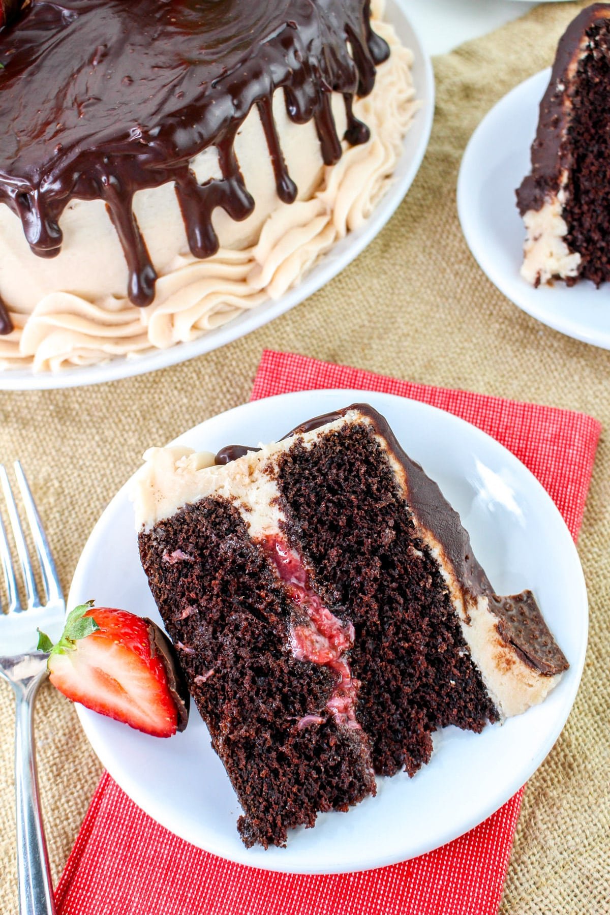 A delectable slice of chocolate-covered strawberry cake sits on a white plate, featuring rich frosting and a delightful strawberry filling, garnished elegantly with a fresh strawberry.