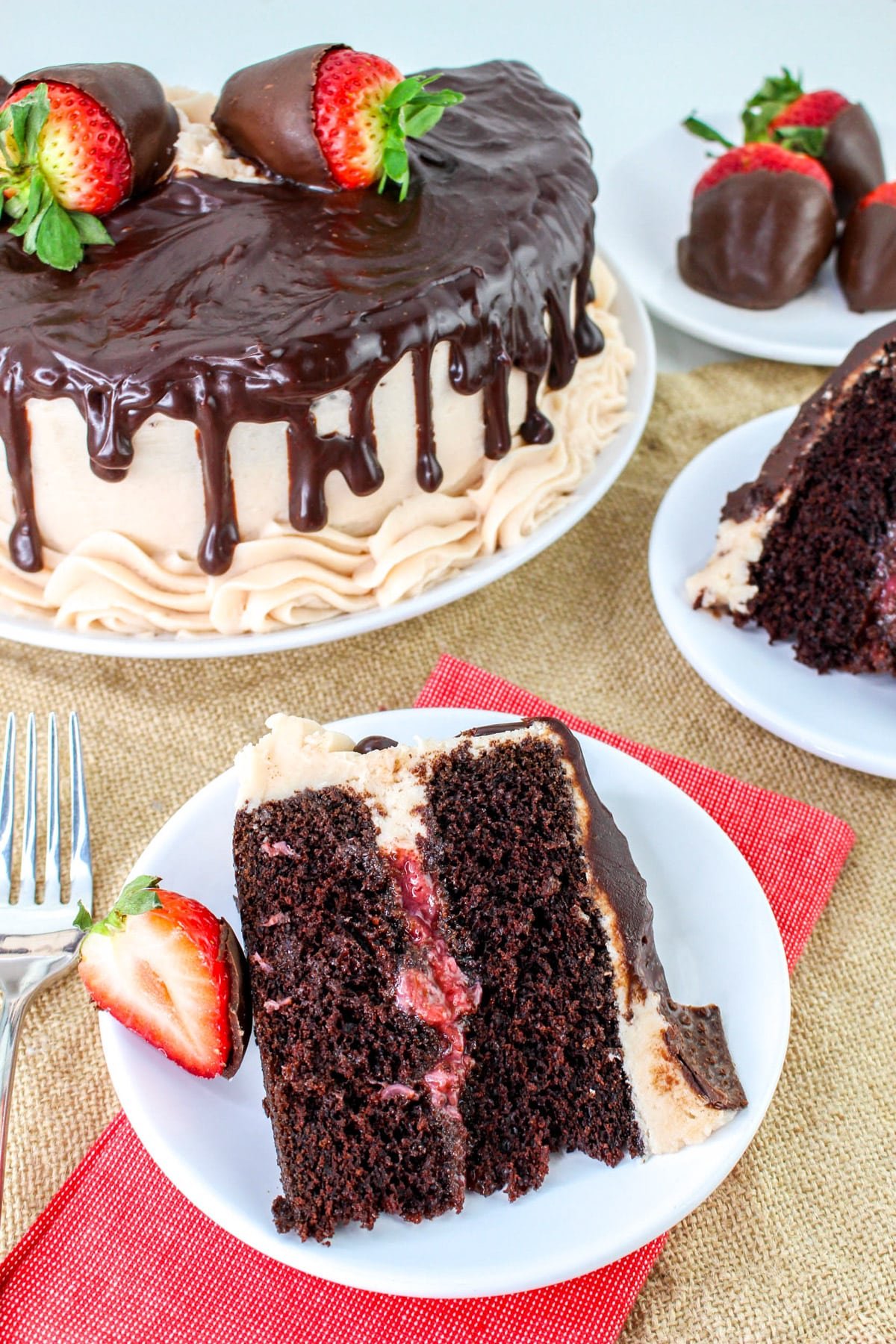 Chocolate cake with strawberry filling, topped with chocolate-covered strawberries, next to a slice on a plate.