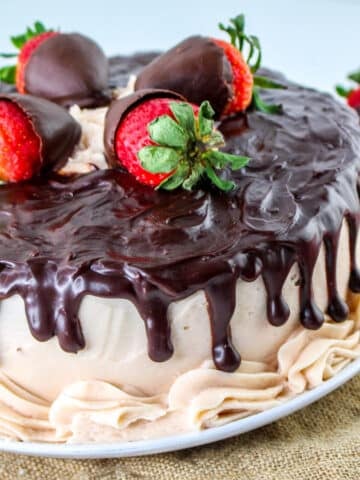 Indulge in a chocolate-covered strawberry cake featuring layers of rich chocolate cake topped with chocolate strawberries, drizzled ganache, and cream frosting, all elegantly presented on a white plate.