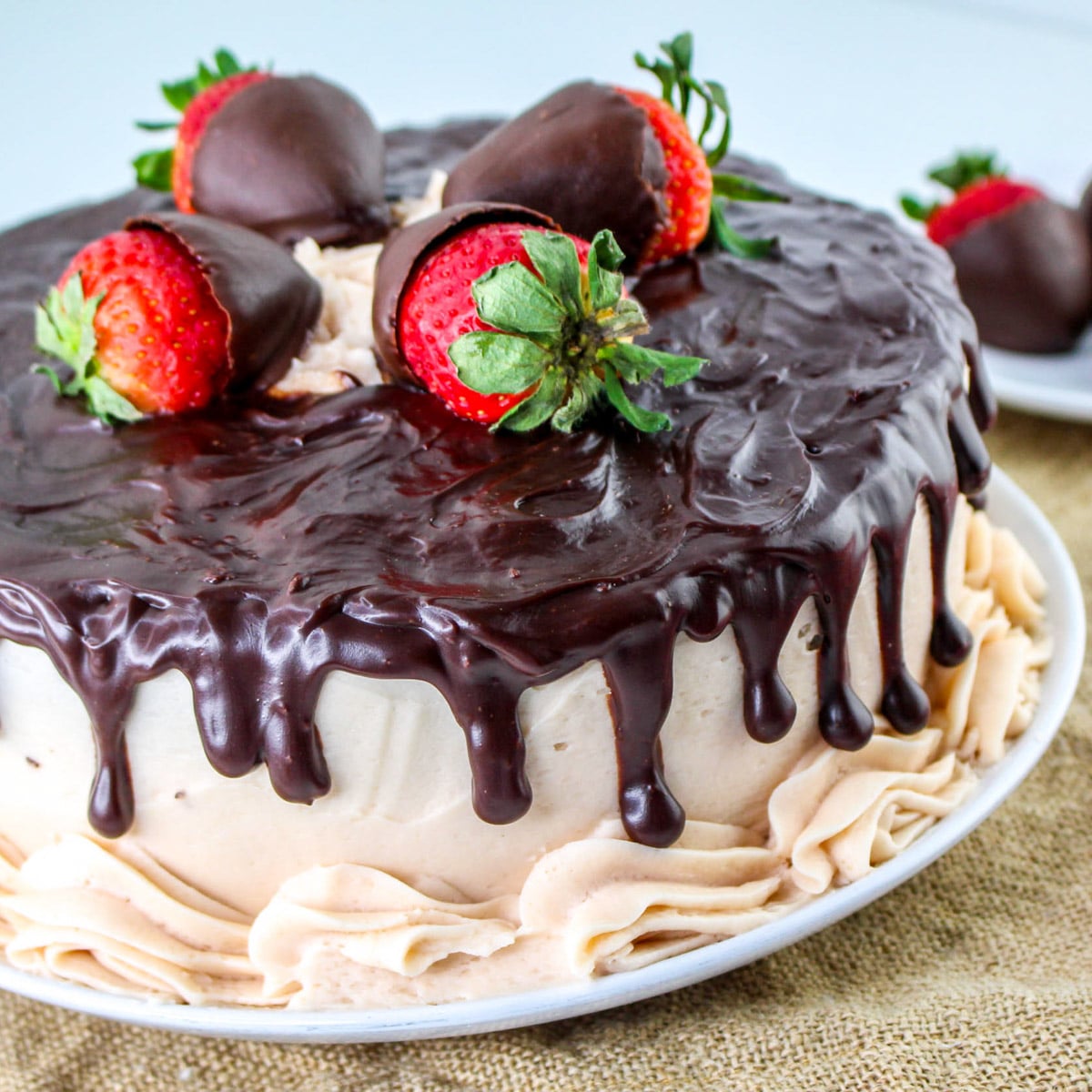 Indulge in a chocolate-covered strawberry cake featuring layers of rich chocolate cake topped with chocolate strawberries, drizzled ganache, and cream frosting, all elegantly presented on a white plate.