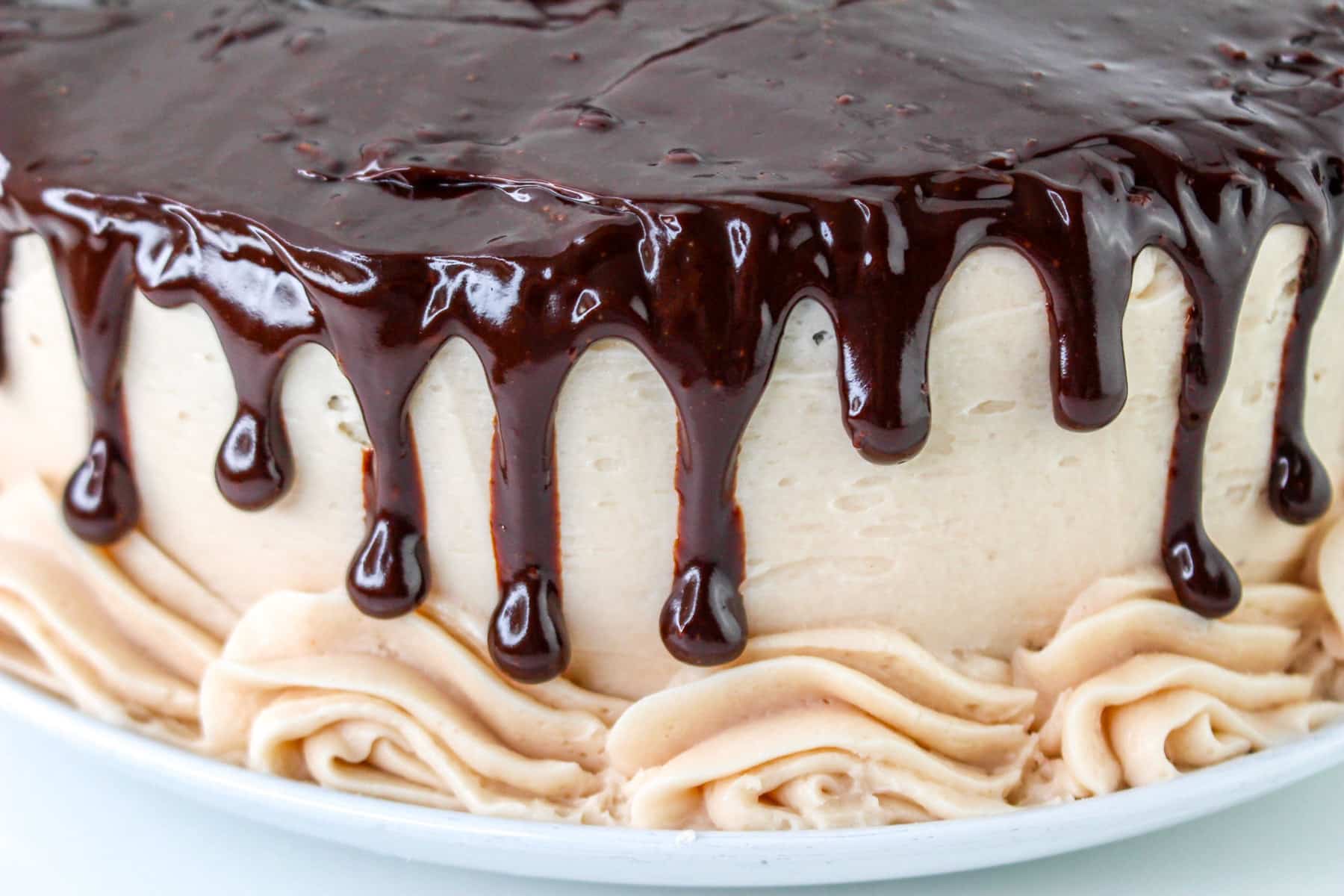 A chocolate covered strawberry cake features luscious ganache dripping down its white frosting with decorative swirls gracefully encircling the base.