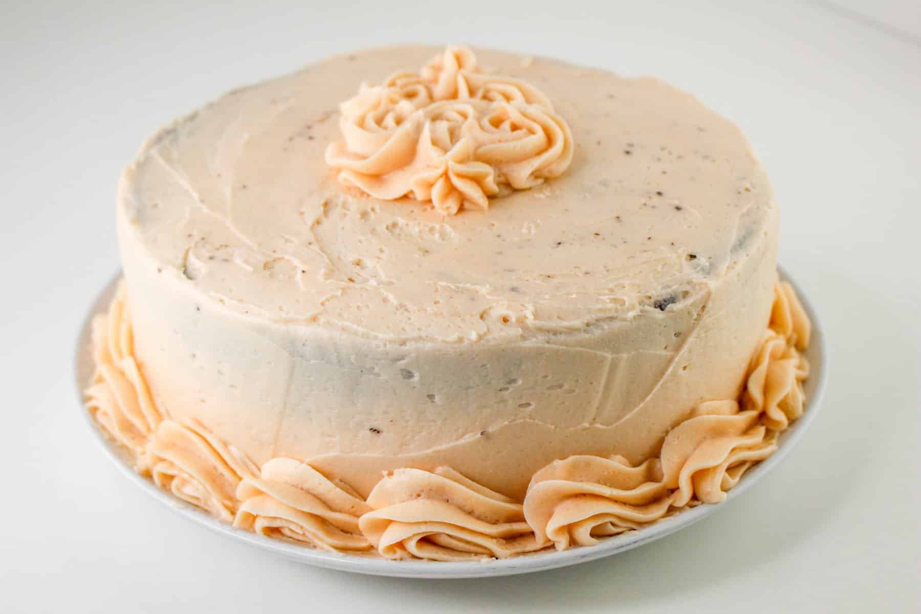 A round cake with light pink frosting and decorative swirls on top and at the base.