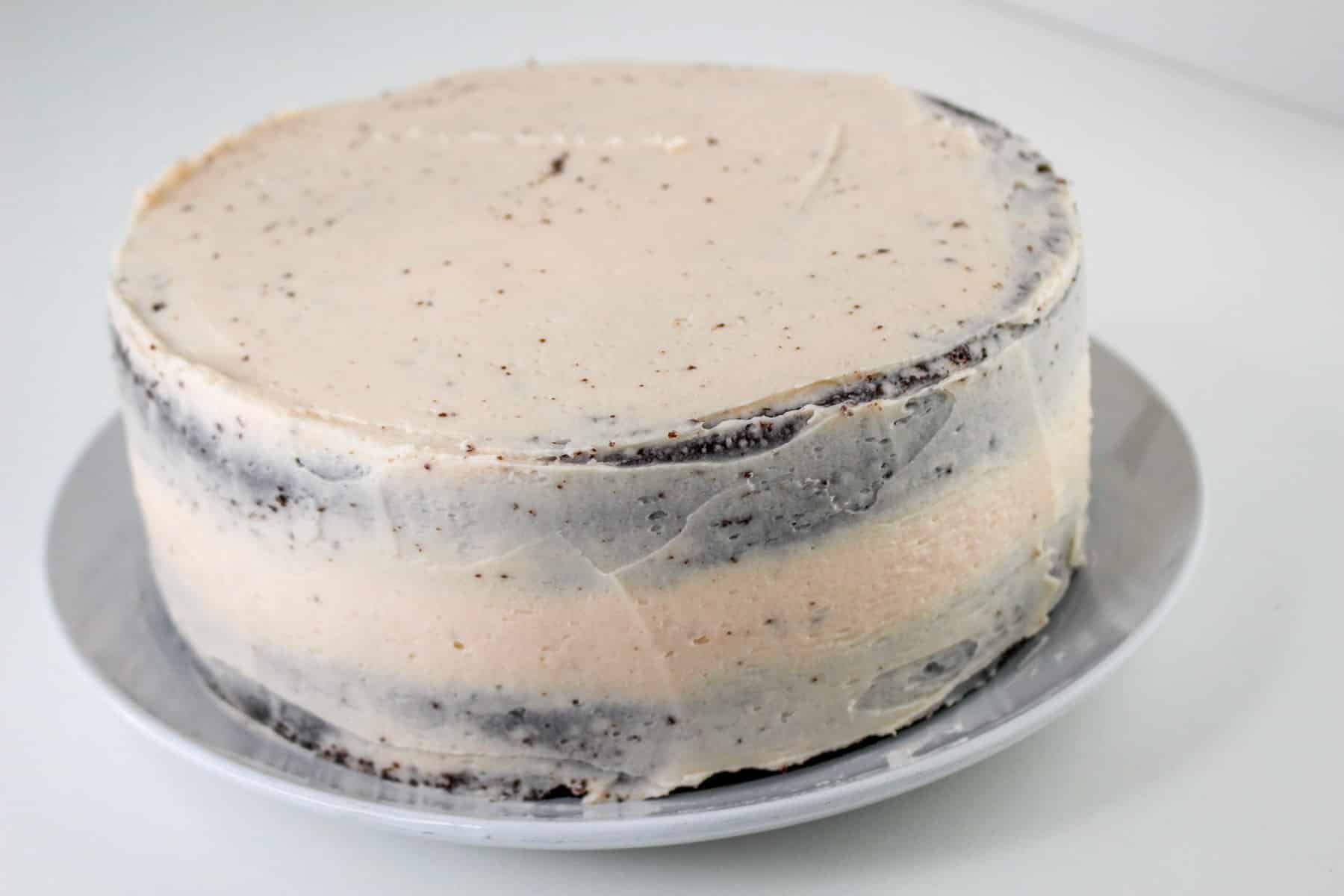 A round, frosted chocolate covered strawberry cake with two visible layers sits elegantly on a white plate, against a plain background.