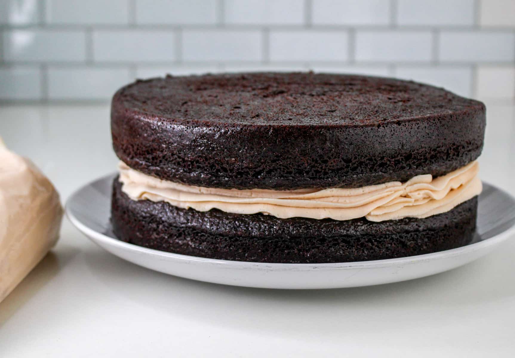 Chocolate covered strawberry cake with a layer of light brown frosting in the middle, resting elegantly on a white plate.