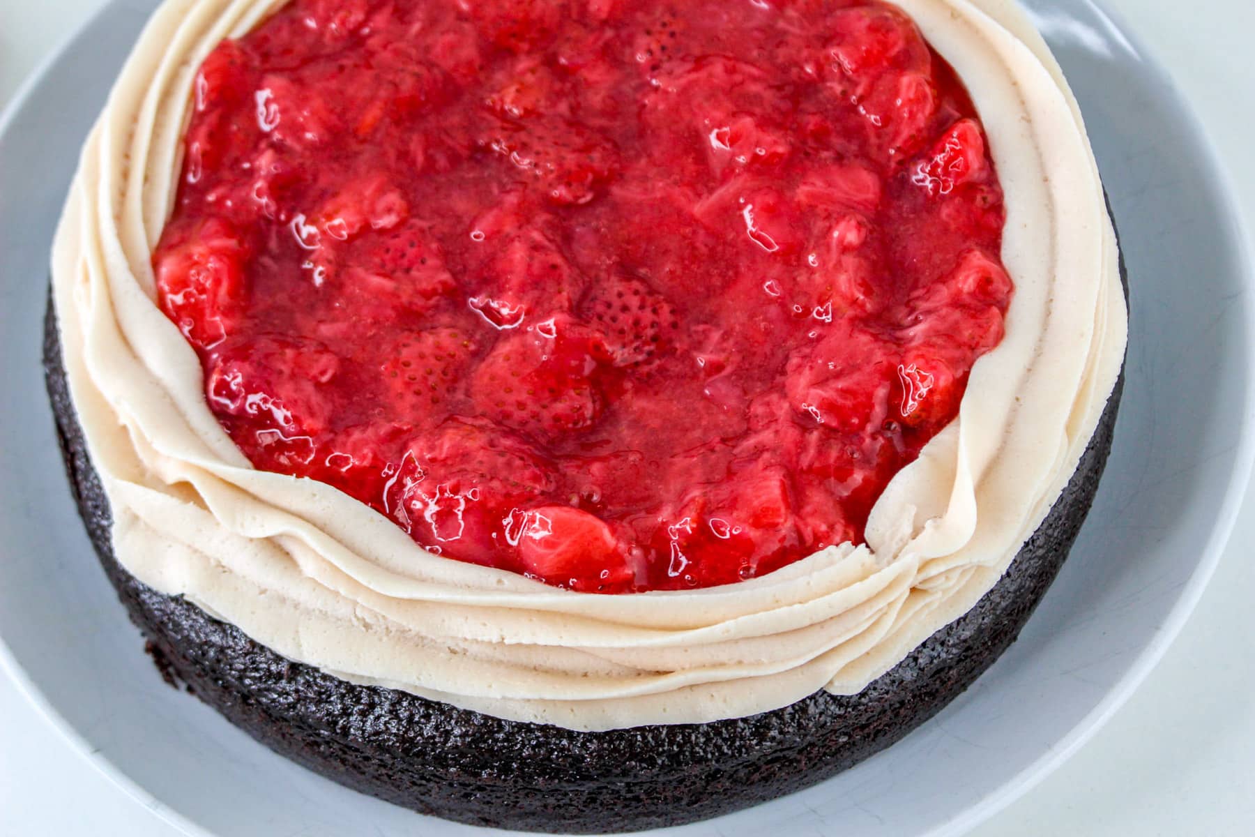 A chocolate-covered strawberry cake features a rich chocolate base topped with a luscious layer of strawberry sauce, all surrounded by light, fluffy frosting.