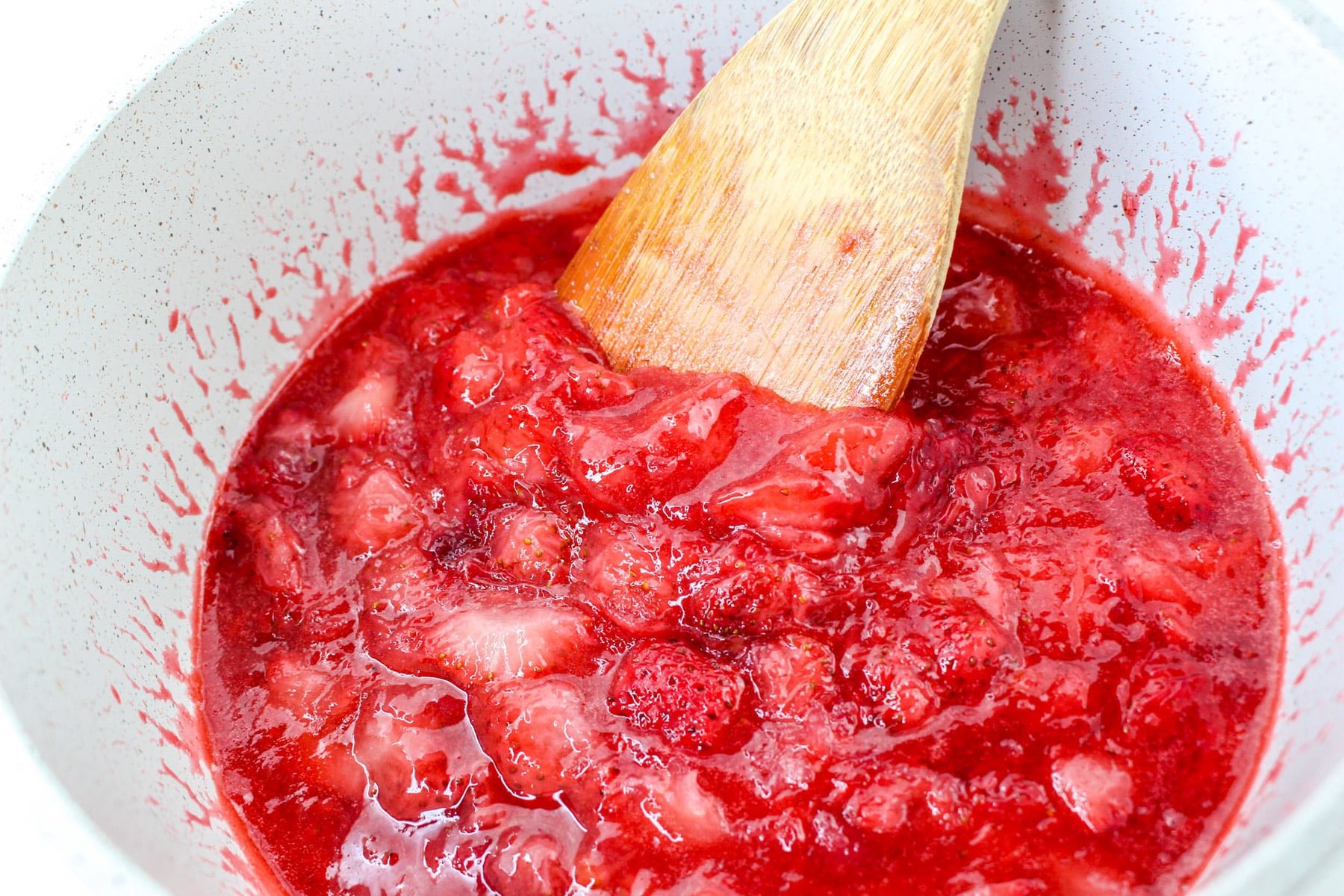 A wooden spoon stirring a pot of fresh, chunky strawberry sauce.