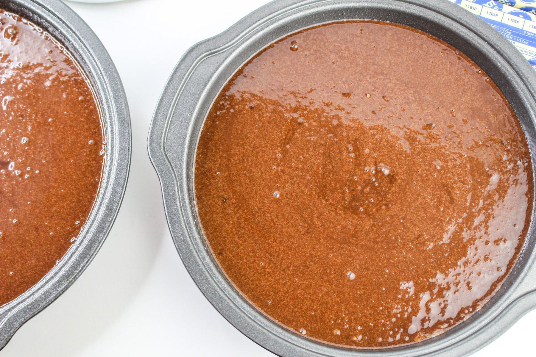 Two round baking pans filled with chocolate-covered strawberry cake batter, ready to be baked.