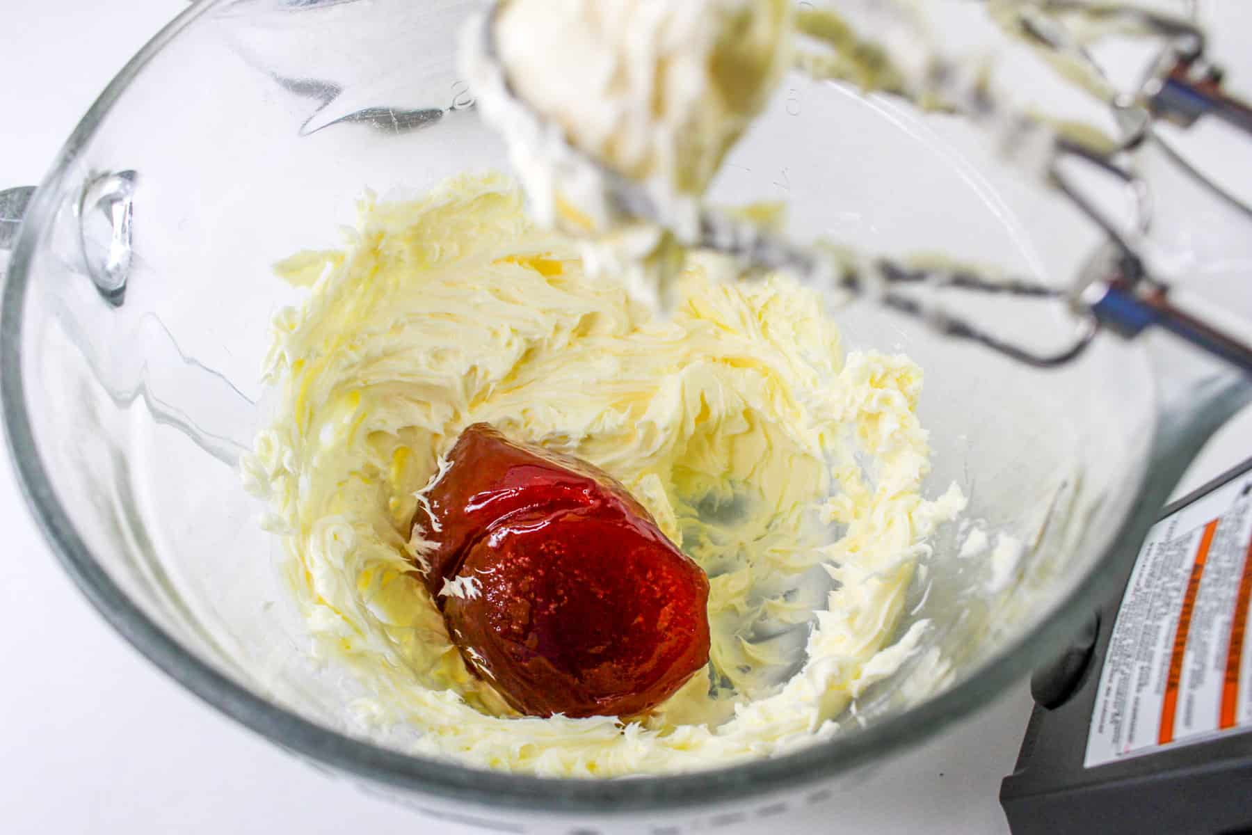 Whipped butter, powdered sugar, and red jam swirl together in a glass bowl.