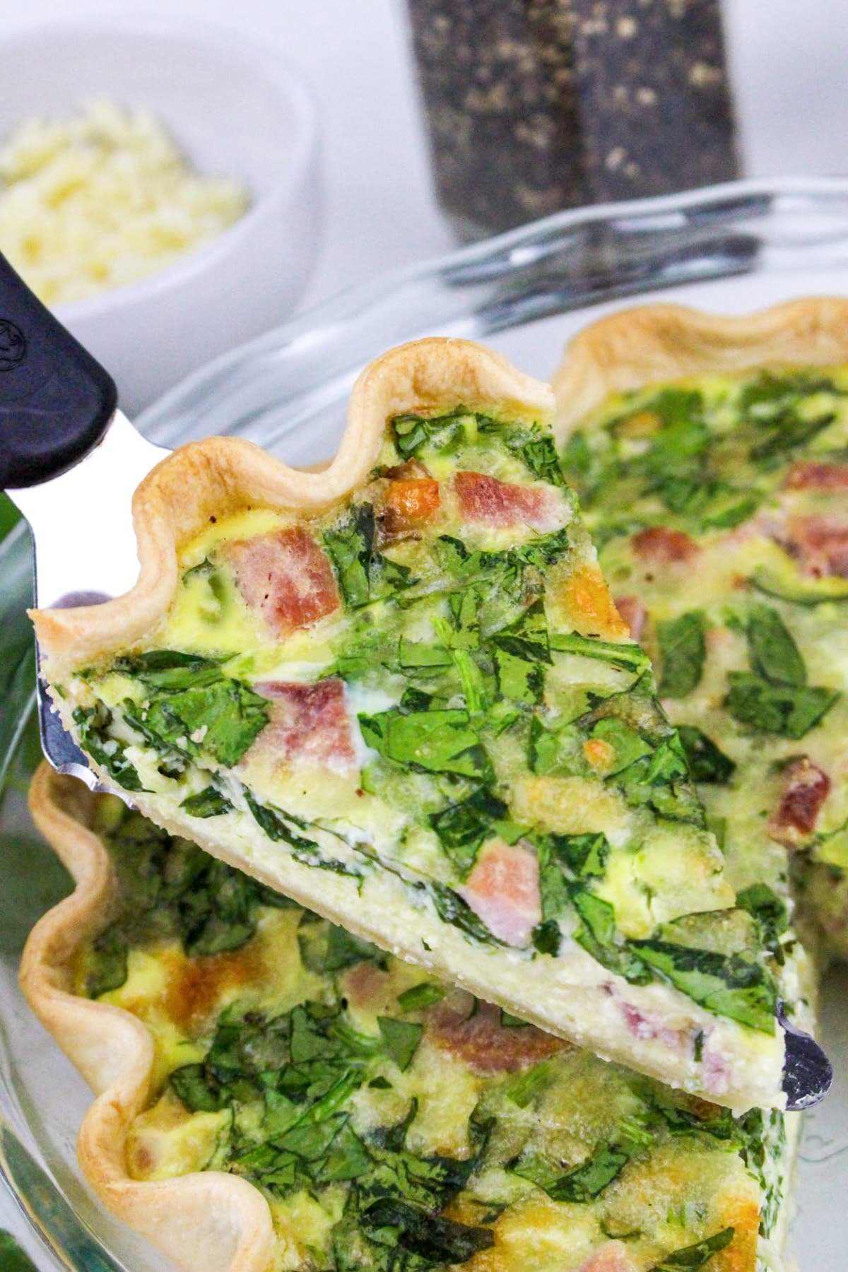 Close-up of a spinach and ham quiche slice being served from a pie dish.