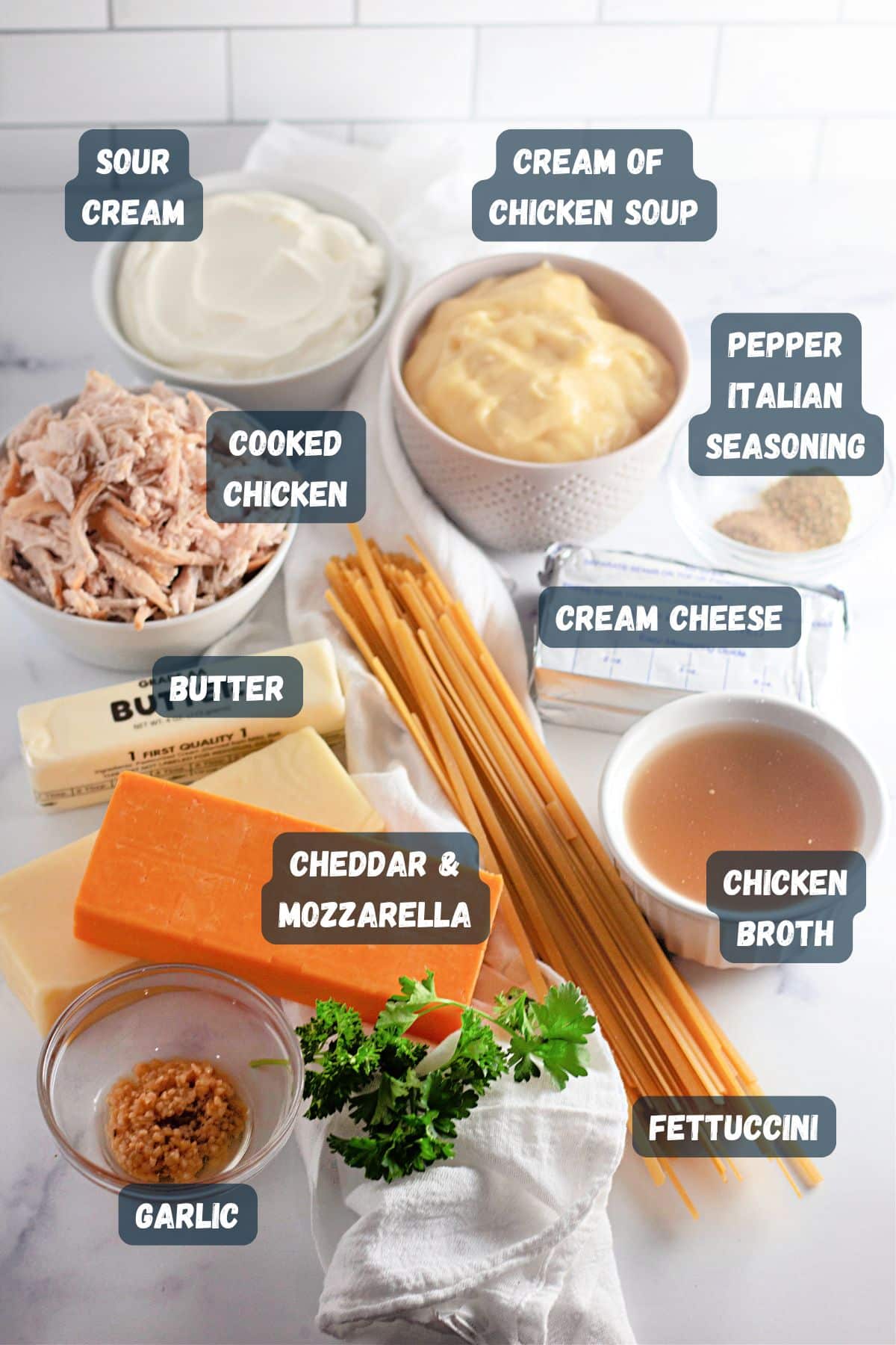 Ingredients laid out for a recipe: sour cream, cream of chicken soup, cooked chicken, butter, cheeses, broth, pasta.