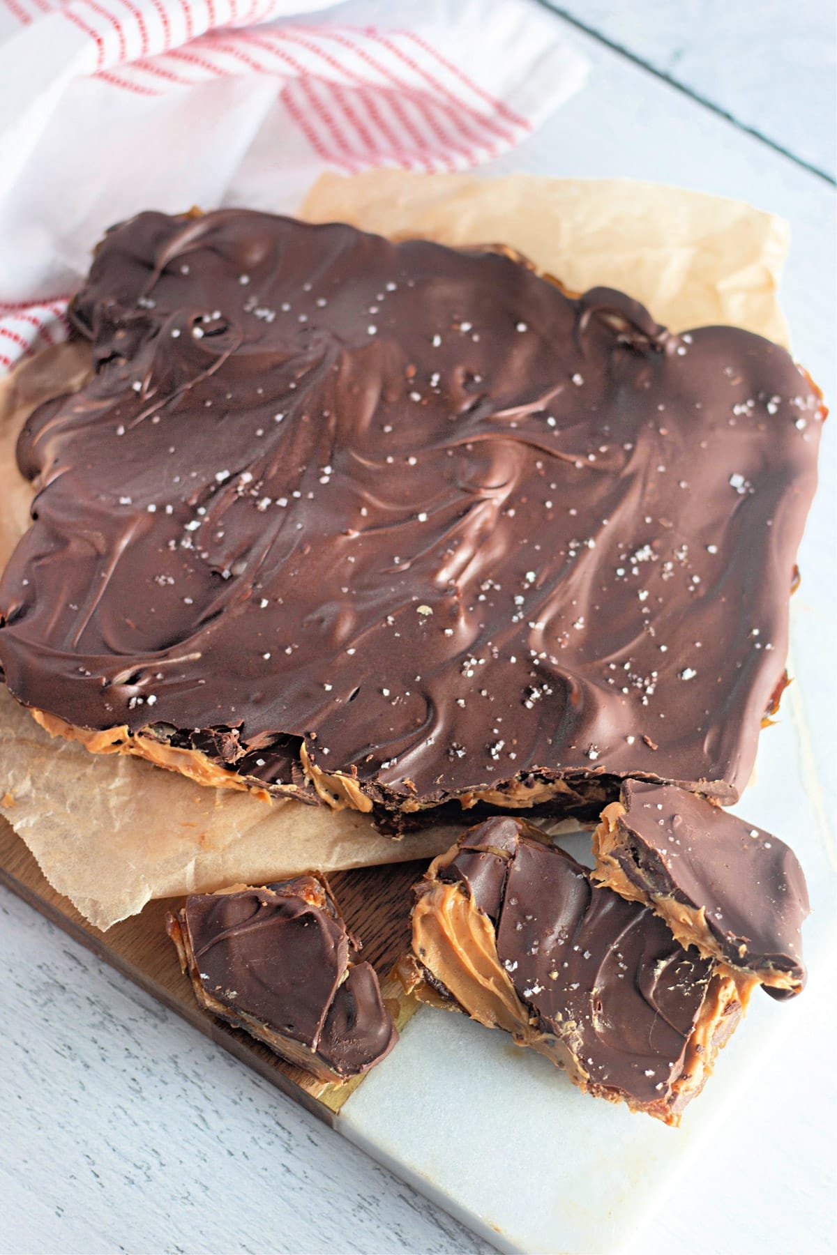 Chocolate-covered toffee with sprinkled salt on a parchment-covered board, with pieces broken off.