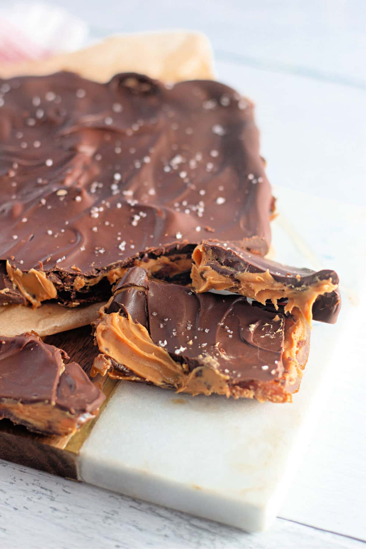 Chocolate-covered crackers with peanut butter and sea salt on a white surface.