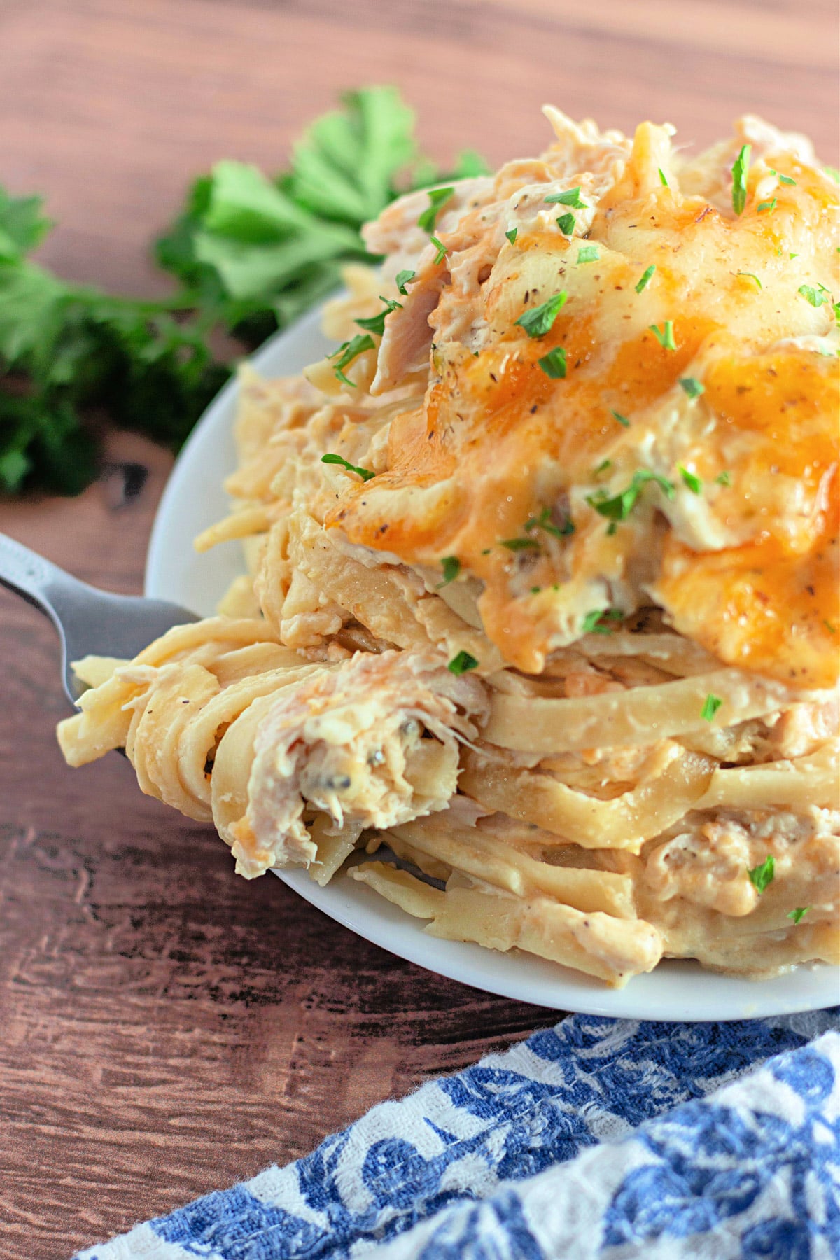 A plate of creamy pasta topped with melted cheese and parsley, with a fork on a wooden table.