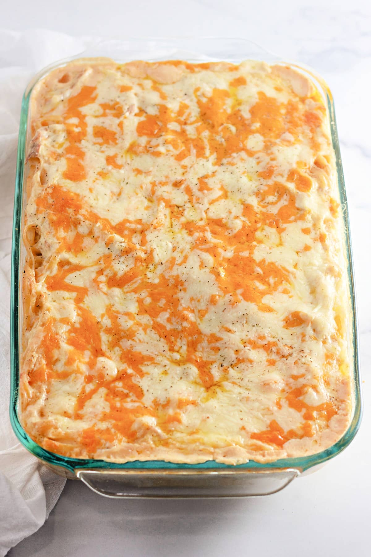 A baked casserole dish with melted cheese on top in a clear glass baking pan.