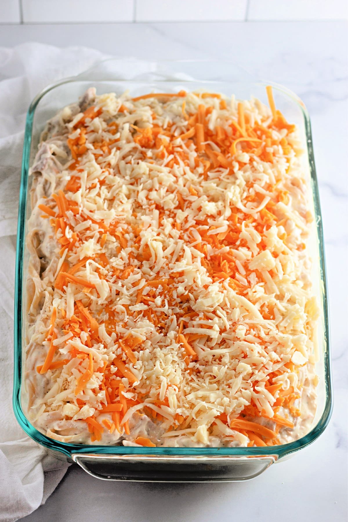 A glass baking dish filled with shredded cheese-topped casserole on a marble surface.