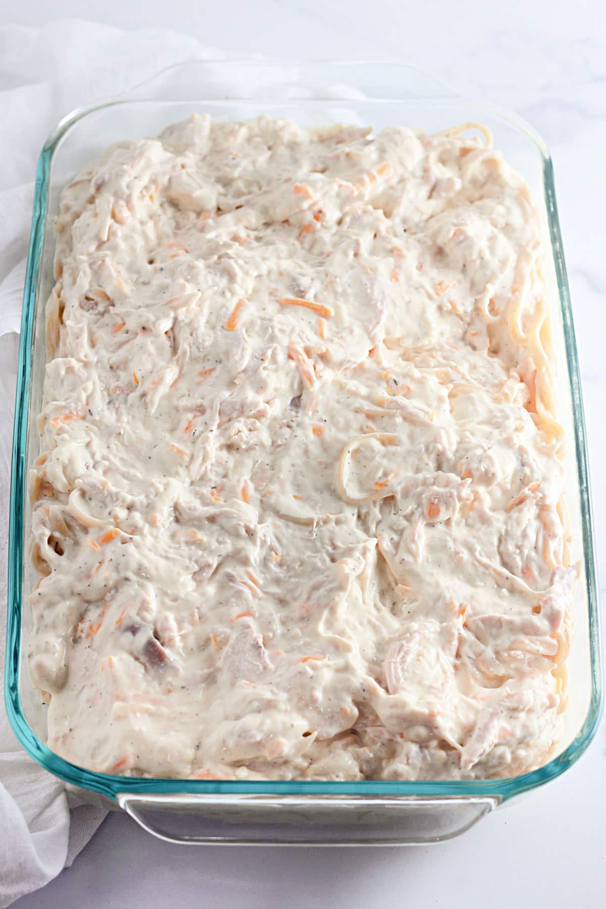 Glass dish filled with creamy chicken spaghetti mixture on a marble surface.