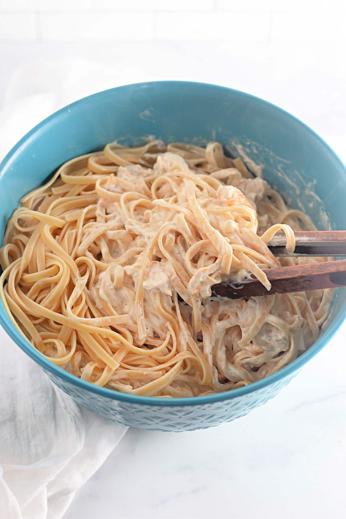 A blue bowl filled with creamy pasta being mixed with wooden utensils.