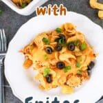 A plate of delicious taco casserole with Fritos, adorned with cheese, olives, and green onions, sits invitingly with a fork on the side.