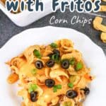 A plate of taco casserole with Fritos, topped with olives and green onions, is surrounded by more Fritos on the table.