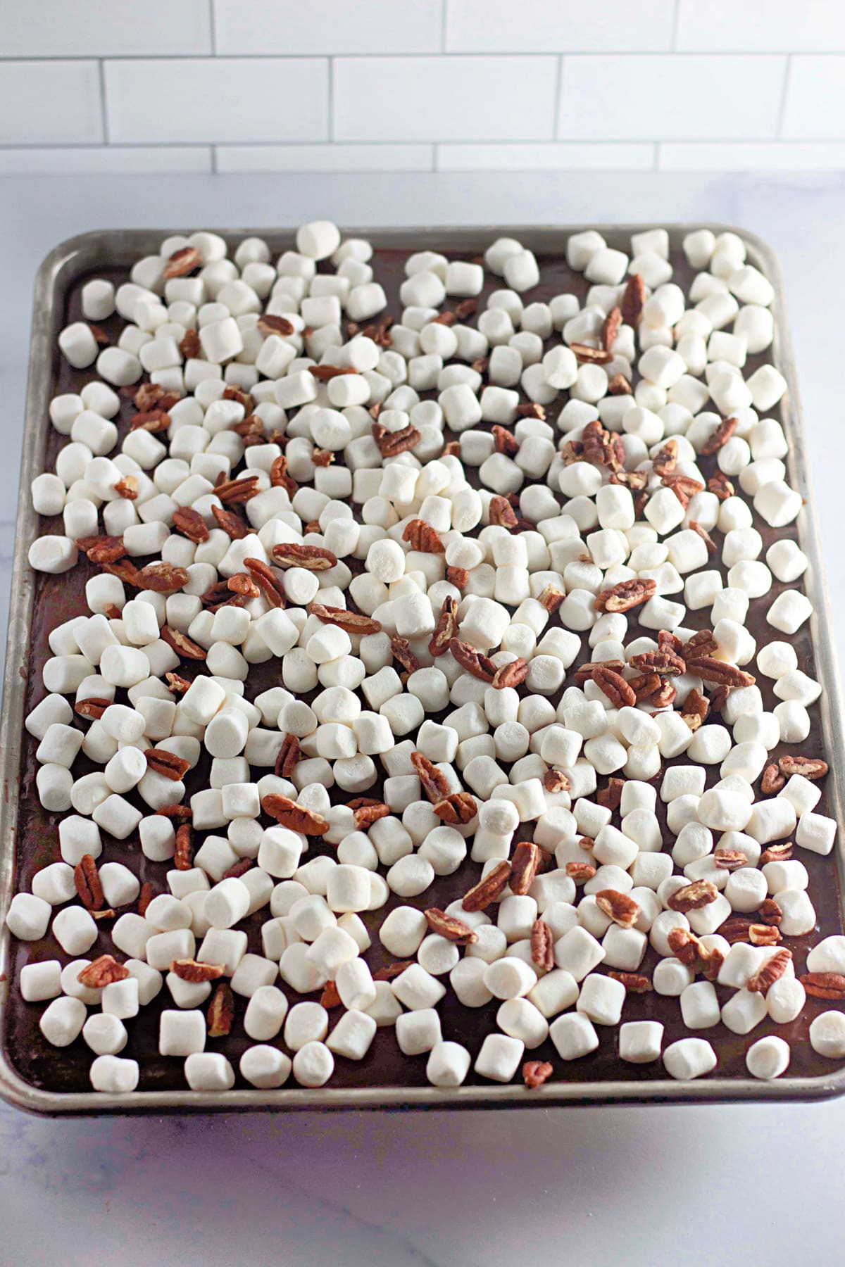 A baking tray with chocolate cake topped with mini marshmallows and nuts.