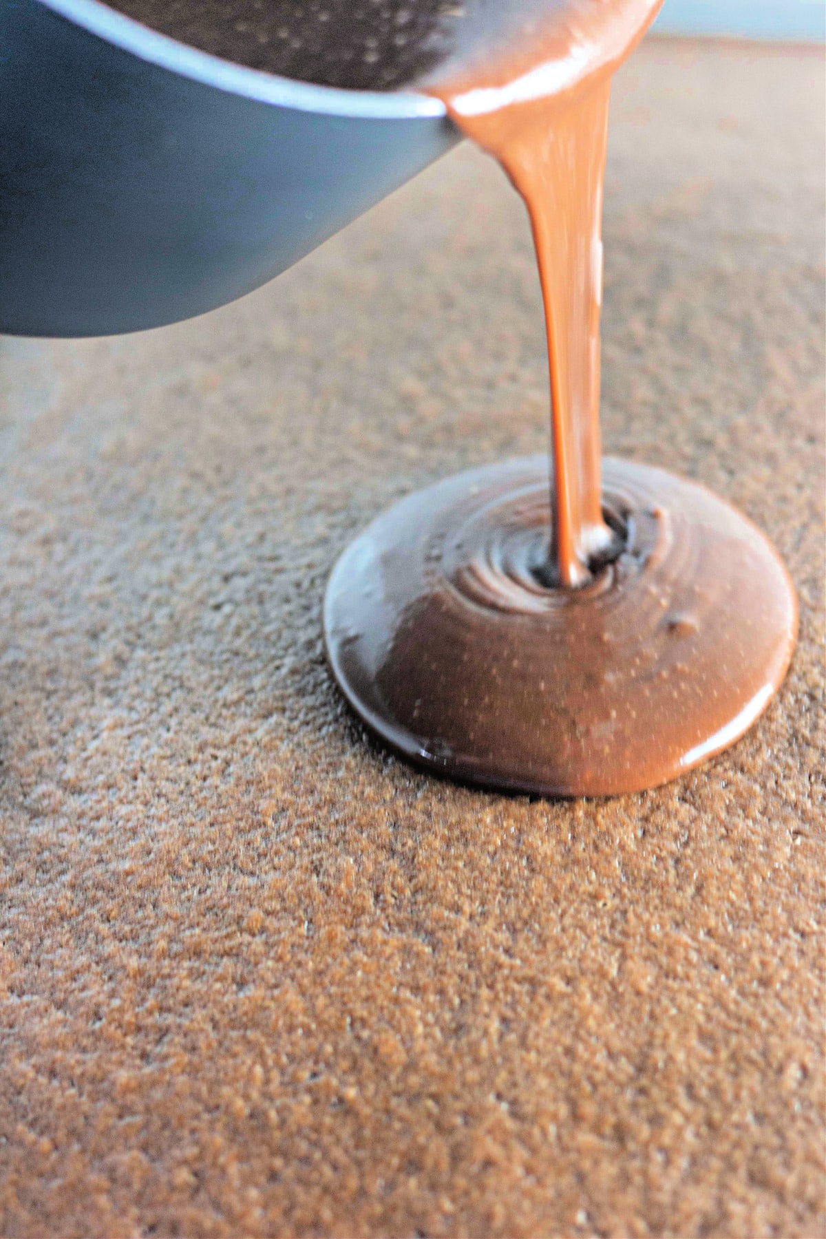 Chocolate being poured from a container, creating a puddle on a textured surface.