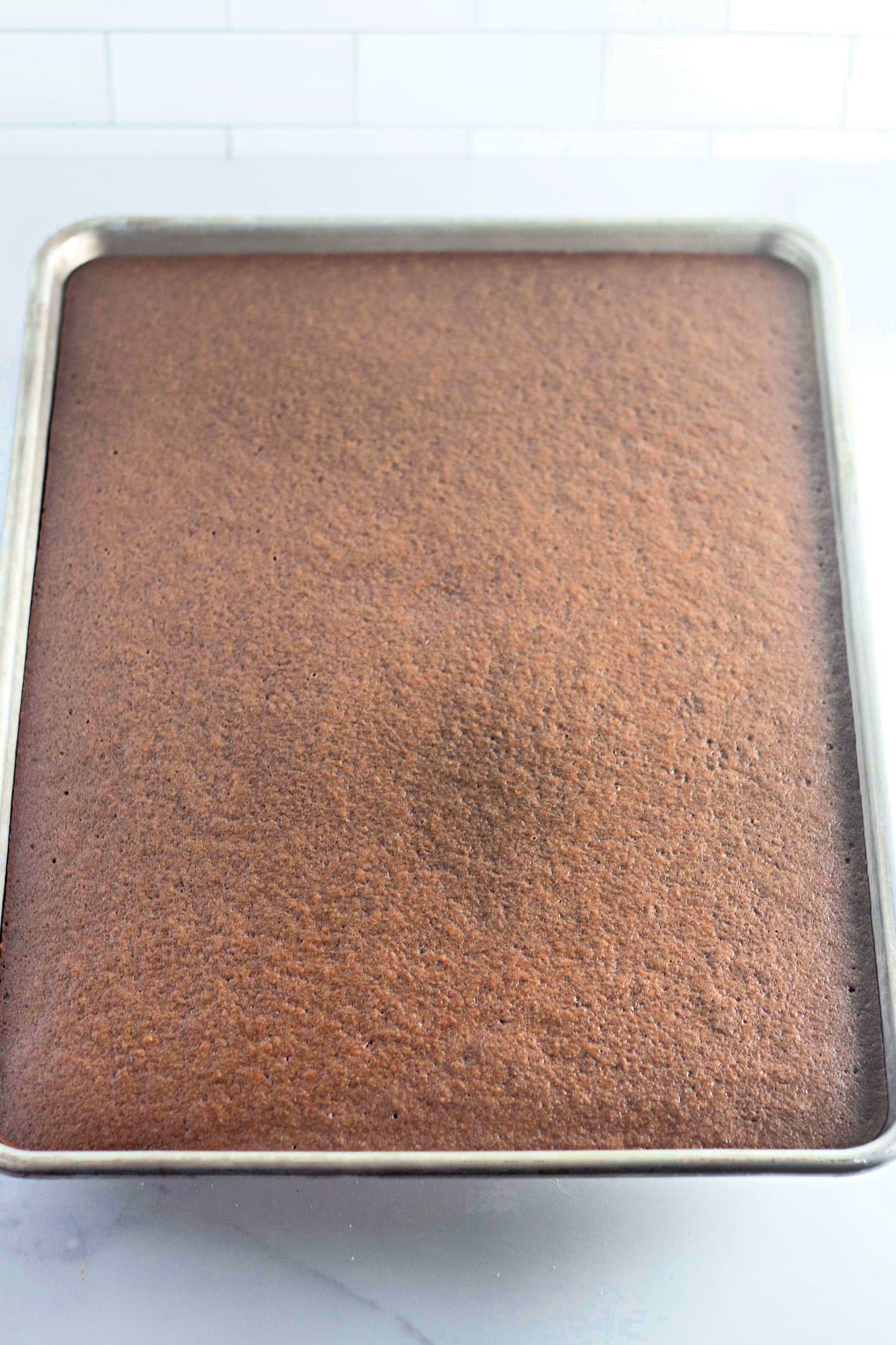 A sheet pan filled with freshly baked chocolate cake on a marble countertop.