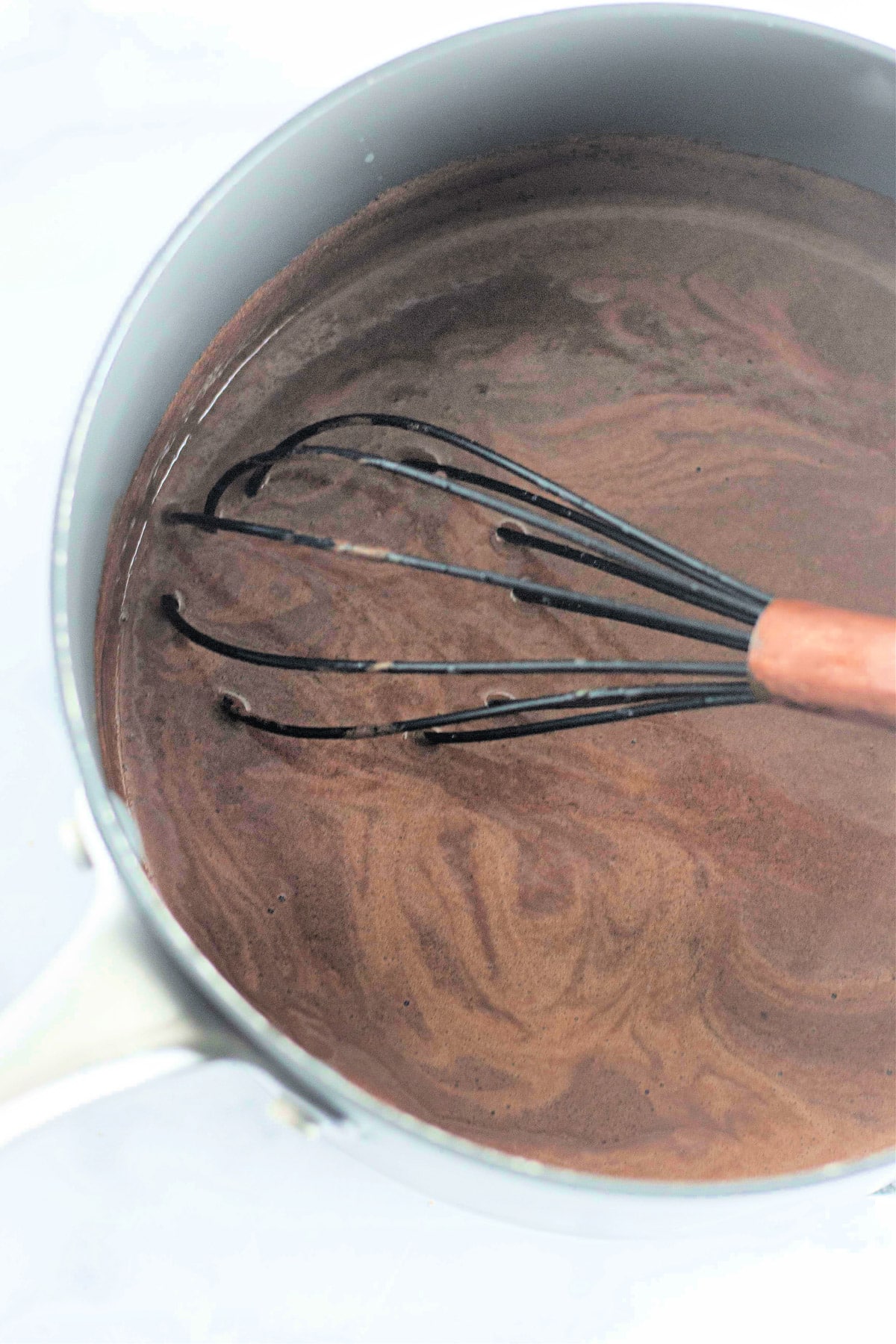 A whisk in a saucepan with swirling chocolate liquid.