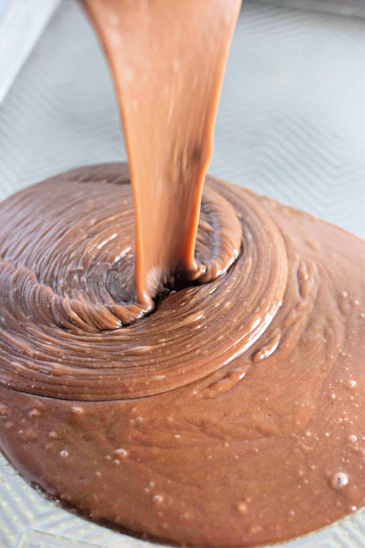 Close-up of smooth, flowing chocolate cake batter being poured into a baking pan.