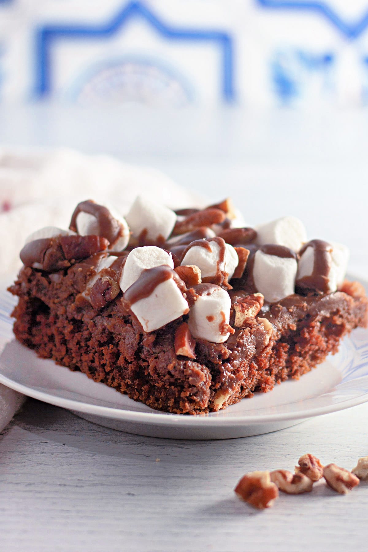 Slice of chocolate cake topped with marshmallows, pecans, and chocolate drizzle on a plate.