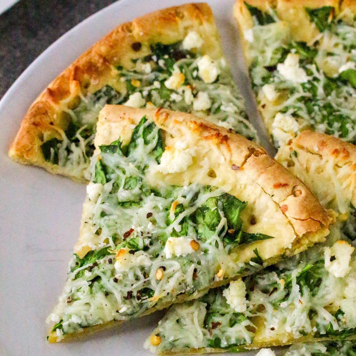 Slices of spinach and cheese pizza on a white plate.